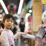 Child holding hands with a robot raising questions about intelligence.