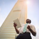 A man standing in front of a corporate building holding a piece of paper with a job offer